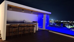 Una cocina moderna con barra, sillas de madera y vistas a la ciudad de noche.