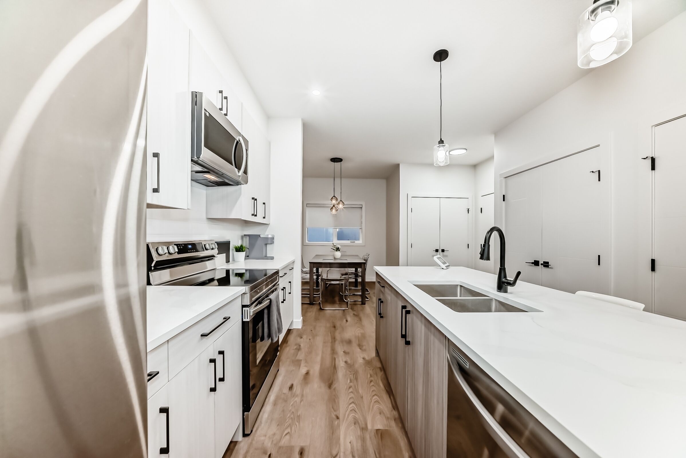 A modern kitchen with white cabinetry, a central island with a sink, and a dining area with a table and chairs.