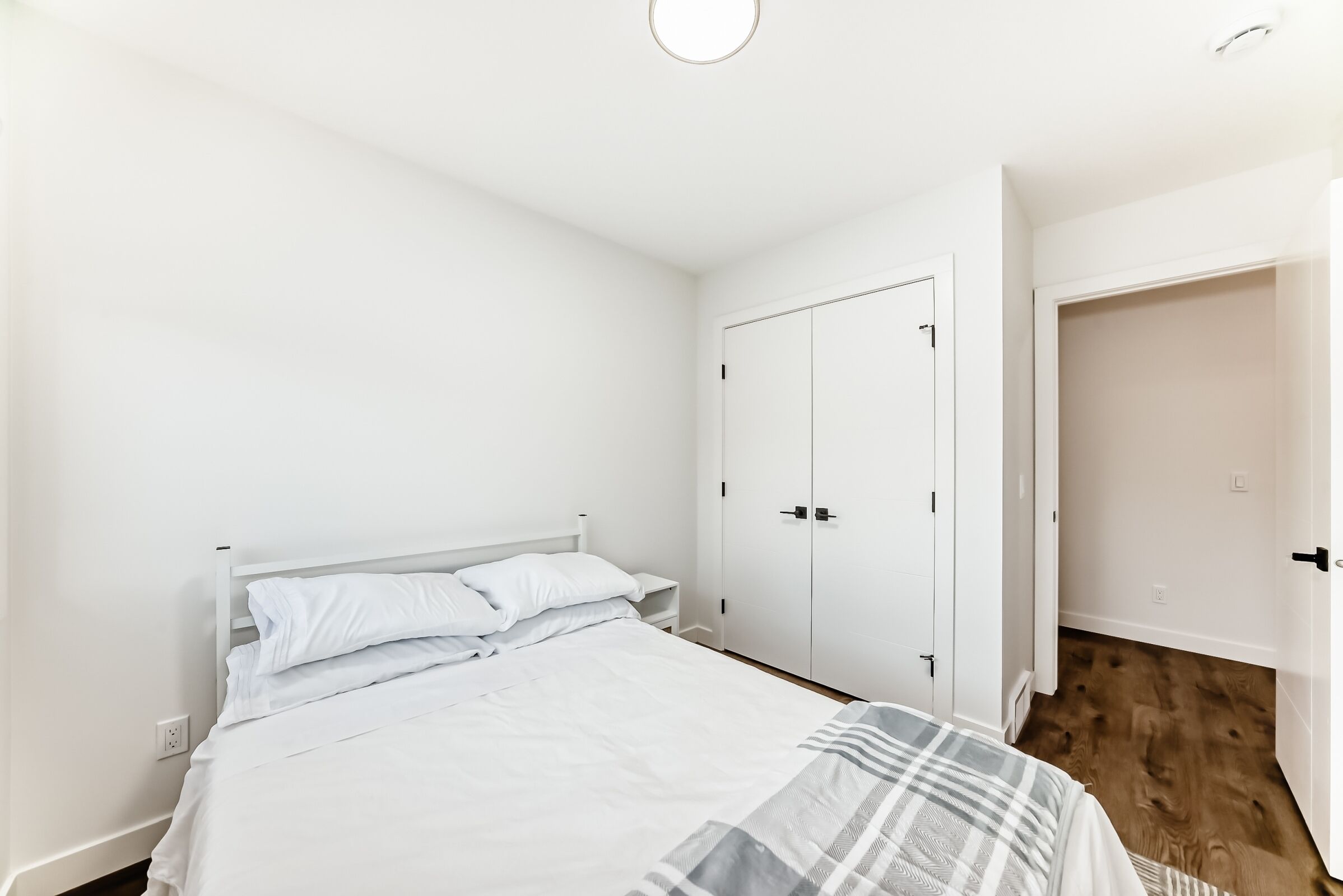 Een slaapkamer met een bed, witte muren, een kledingkast en een houten vloer.