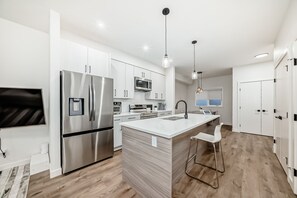 A modern kitchen with stainless steel appliances, a central island, and pendant lighting. - Modern 3BR Townhome | Free Parking | Quartz Kitchen | Family-Friendly (Calgary)
