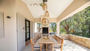 An outdoor patio with a wooden table and chairs, a hanging light fixture, and a stone wall. - Villa La Fourmilière heated pool walking distance to beach (Lecci)