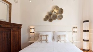 A neatly arranged bedroom with a large bed, bedside lamps, a decorative wall piece, and a tall floor lamp. - Villa La Fourmilière heated pool walking distance to beach (Lecci)