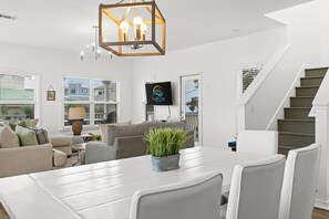 Ein modernes Wohnzimmer mit Esstisch, Sofas, Fernseher und einer Treppe.