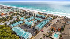 A coastal hotel with multiple buildings, a parking lot, and a beach view.