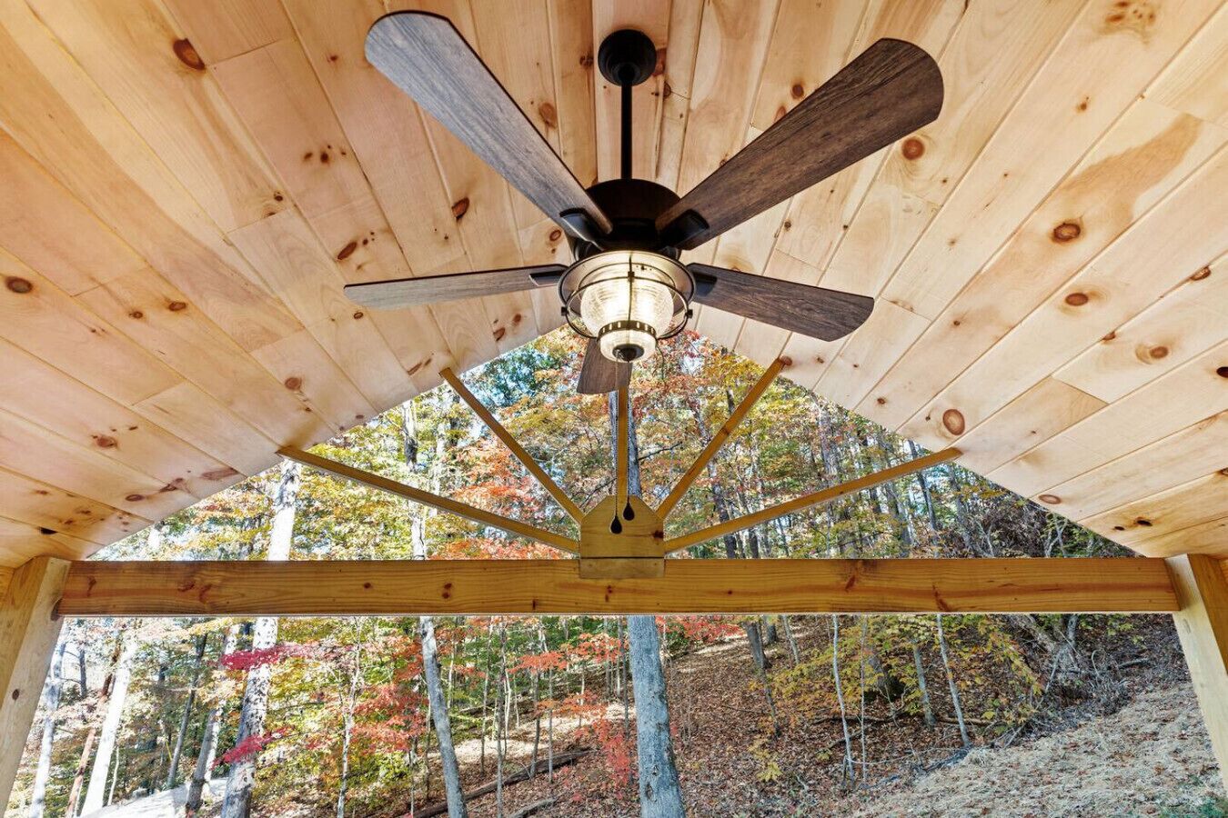 Un ventilador de techo en una cabaña de madera con vistas a un bosque.