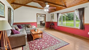Un salon spacieux doté d’un plafond en bois, d’une grande fenêtre avec des rideaux, d’un canapé, d’une table basse et d’un tapis à motifs.