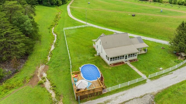 Une grande maison avec un jardin clos, une piscine et une vue sur un champ verdoyant et des collines boisées.