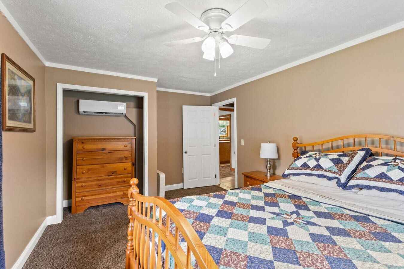 A bedroom with a wooden bed, a ceiling fan, a dresser, and a door leading to another room.