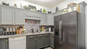 A modern kitchen with grey cabinets, a stainless steel refrigerator, and a tiled backsplash. - Stylish 2BR Townhome w/ Garage & Patio Perfect for Stays or Assignments (Clarksville)