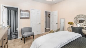 A bedroom with a bed, a chair, a dresser, a vanity with a mirror, and a door leading to another room. - Stylish 2BR Townhome w/ Garage & Patio Perfect for Stays or Assignments (Clarksville)