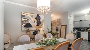 A dining room with a wooden table, six chairs, a chandelier, a painting, and a kitchen in the background. - Stylish 2BR Townhome w/ Garage & Patio Perfect for Stays or Assignments (Clarksville)