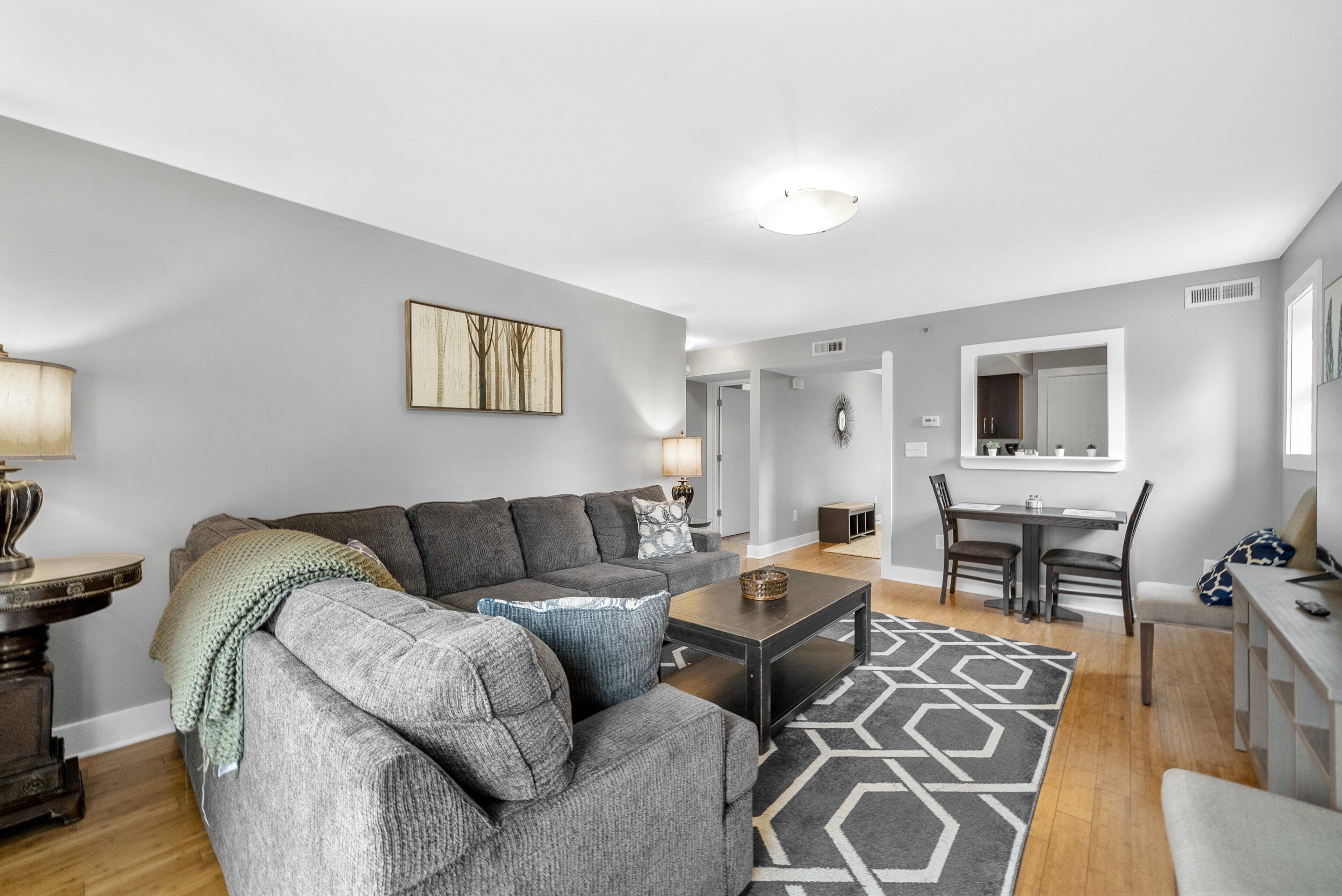 A modern living room with a grey sofa, a coffee table, and a dining area with a table and chairs.