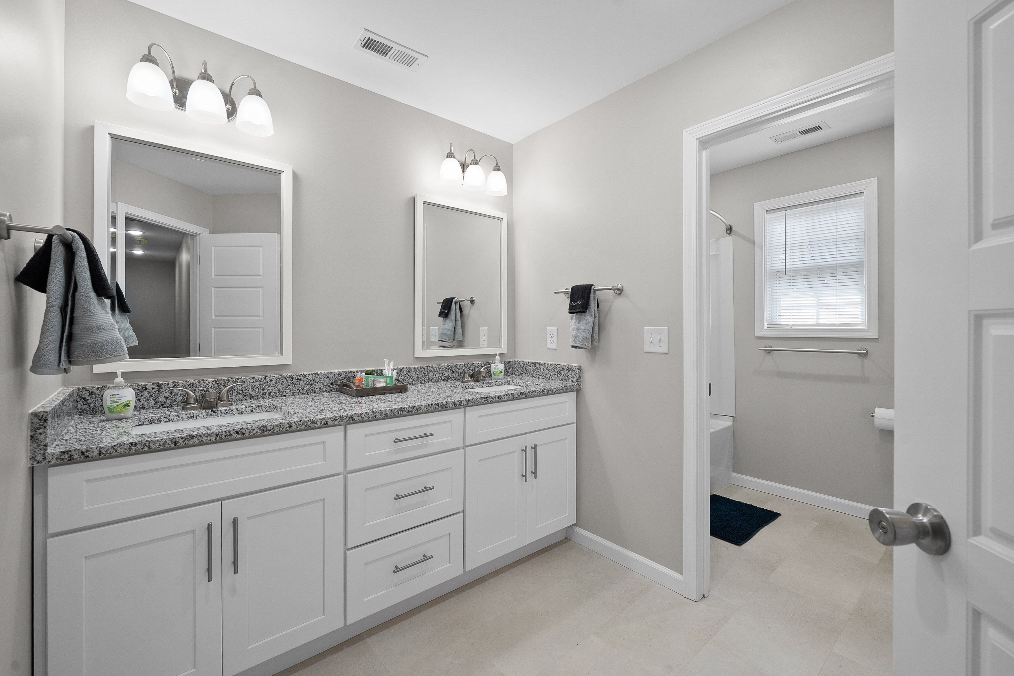A modern bathroom with a granite countertop, white cabinetry, a large mirror, and a walk-in shower.