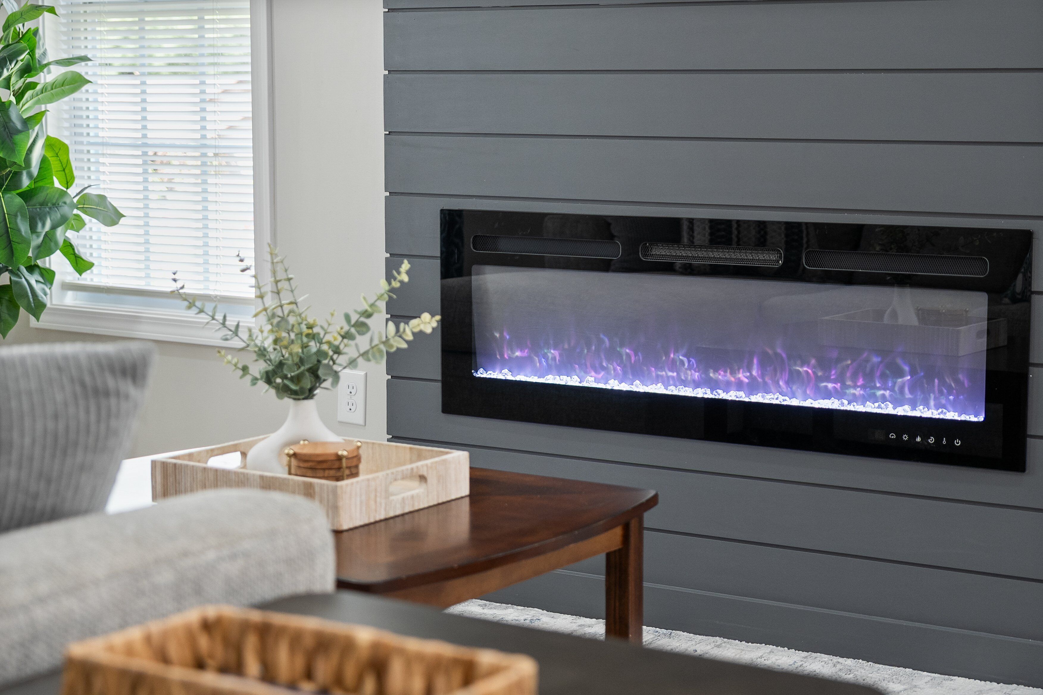 A modern living room with a built-in fireplace, a grey sofa, a wooden coffee table, and a plant.
