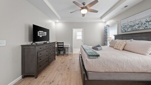 Una camera da letto con un letto, una cassettiera, una scrivania, una sedia, una ventola a soffitto e una TV.