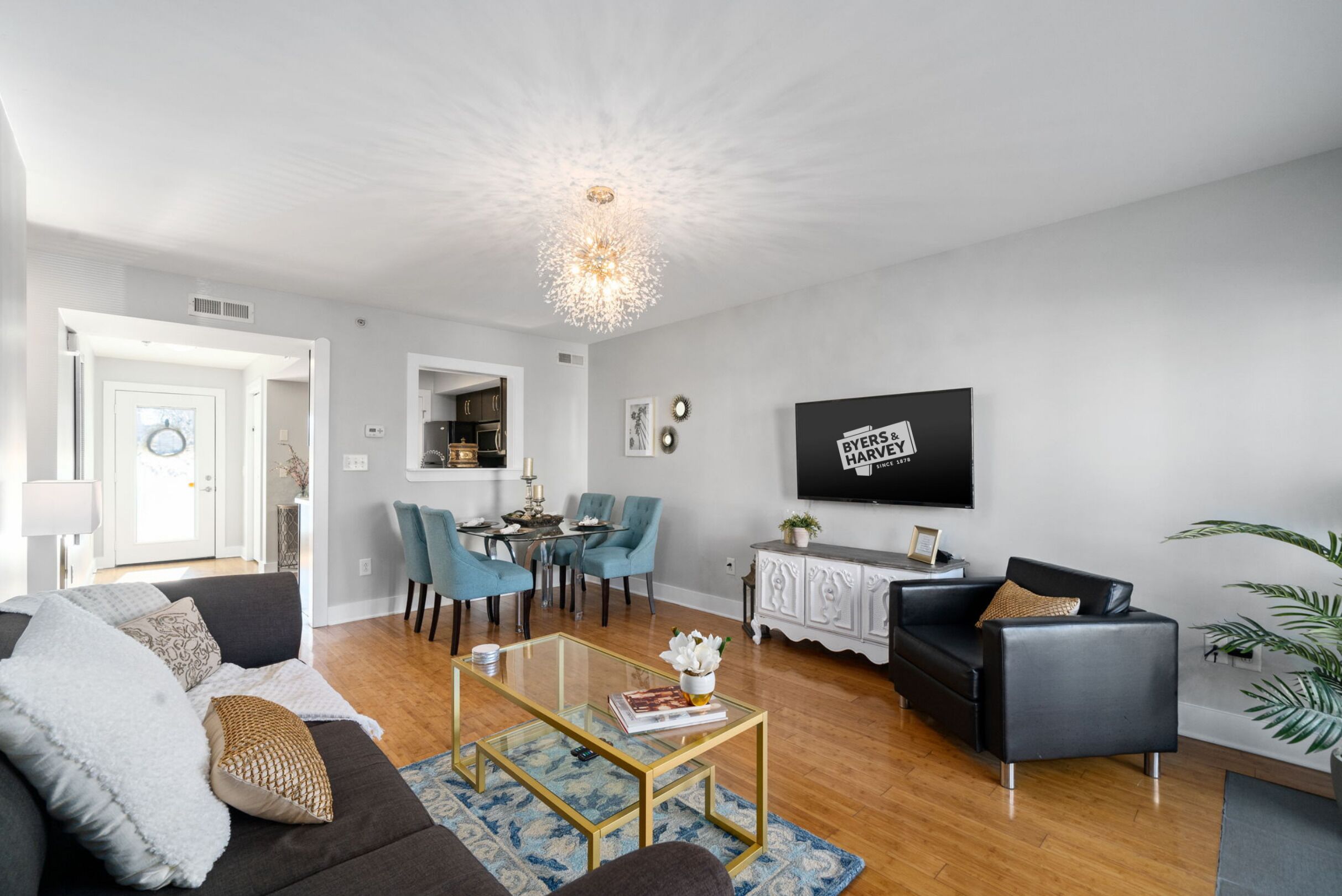 A modern living room with a sofa, coffee table, and TV. There is a dining area with chairs and a table.