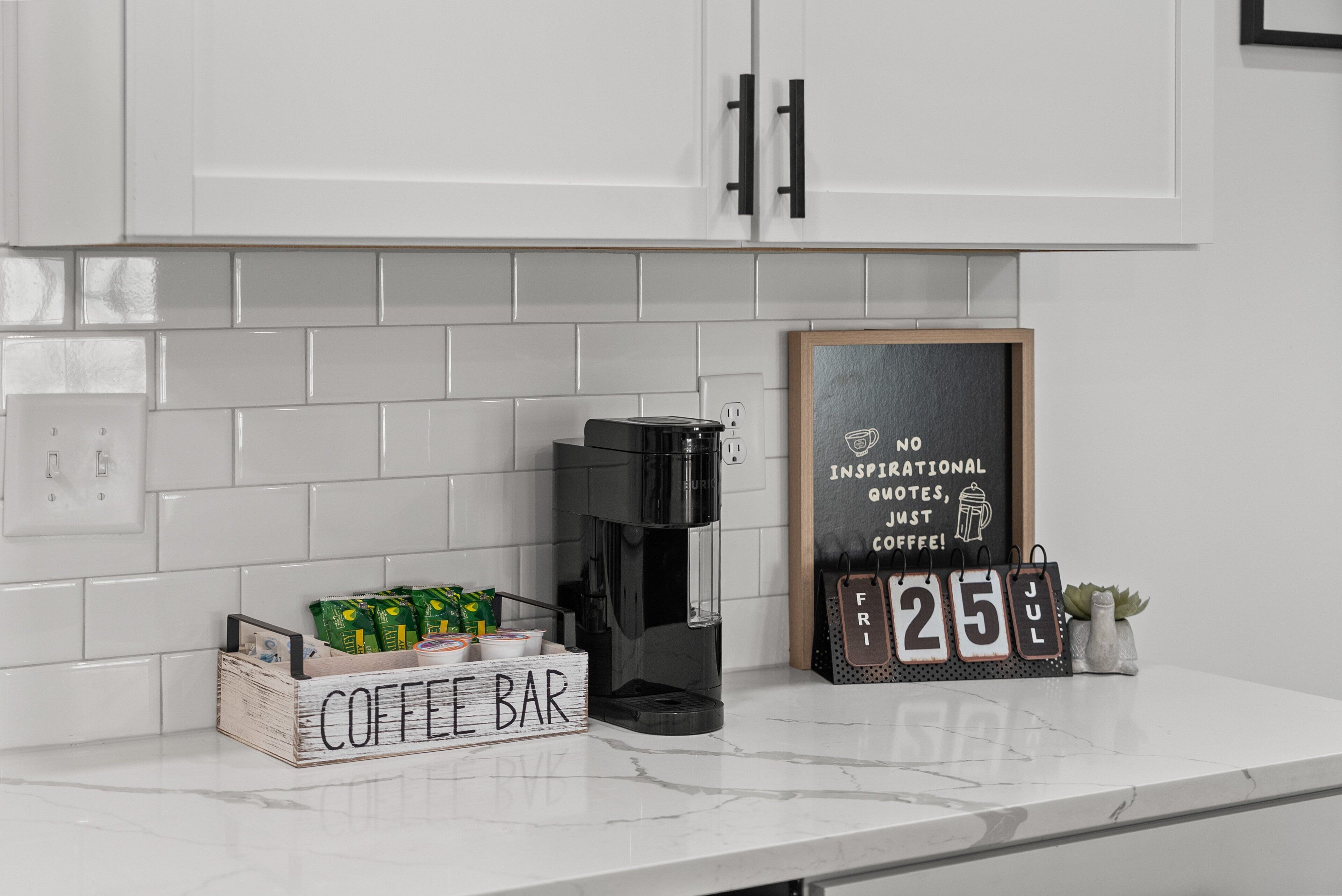 A kitchen counter with a coffee maker, a coffee bar sign, and a chalkboard with motivational writing.