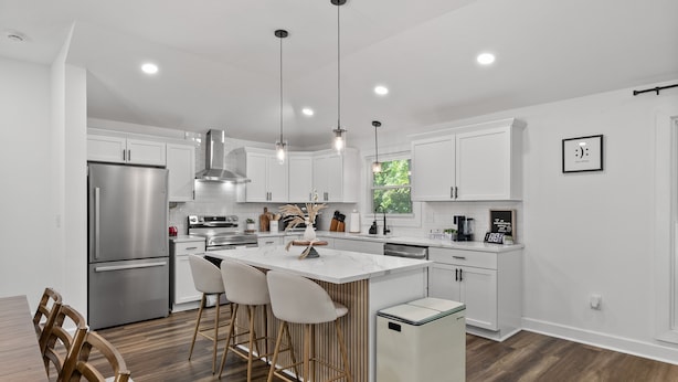 A modern kitchen with white cabinetry, stainless steel appliances, and a central island with bar stools. - Bertin's Place (Clarksville)
