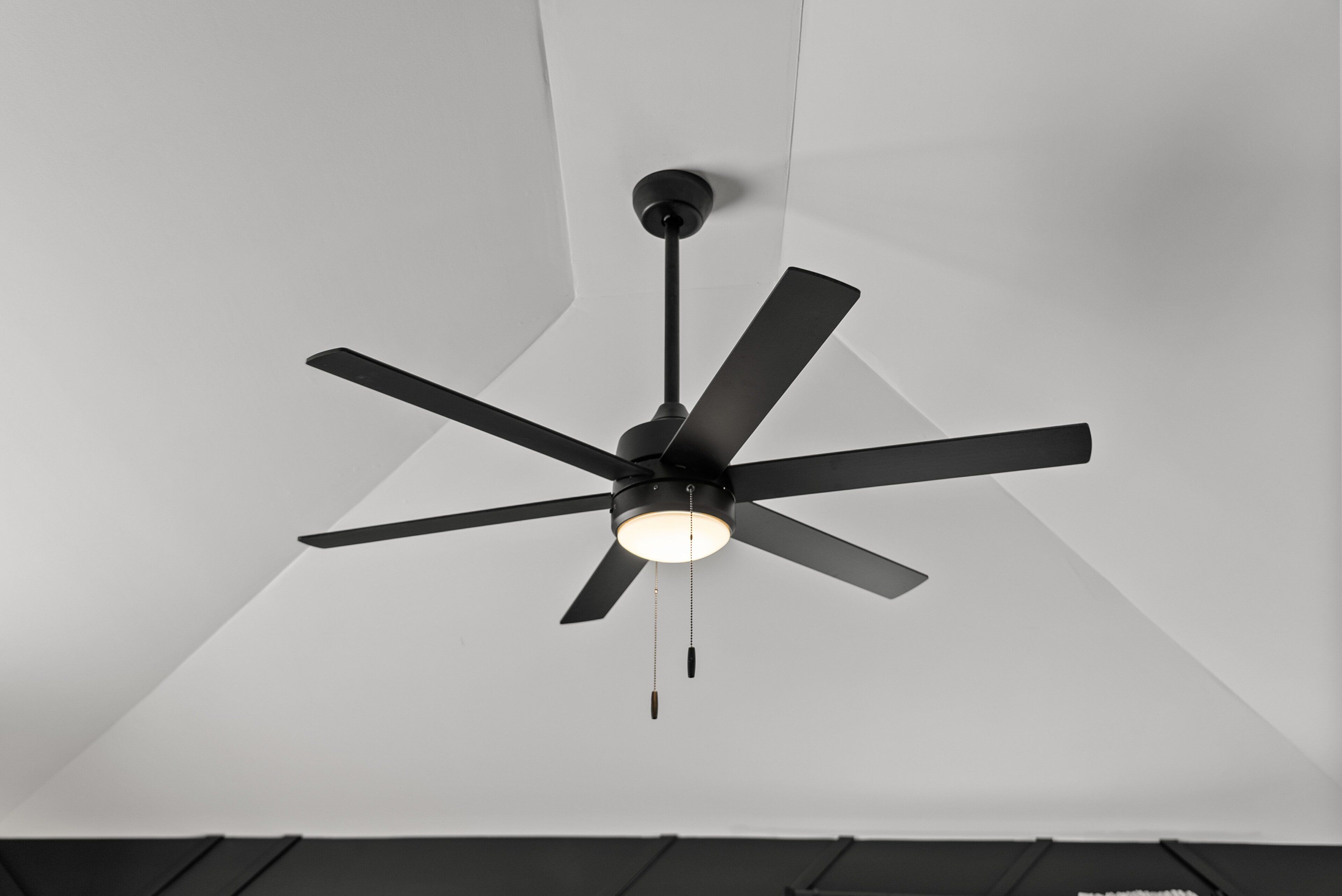 A ceiling fan with a light fixture in a room with white walls and a dark ceiling.