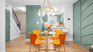 A dining area with a round glass table, four orange chairs, and a chandelier. - Emerald Horizon 104 Azalea Ct (Clarksville)