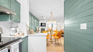 A modern kitchen with teal cabinetry, a central island with orange chairs, and a dining area with a chandelier. - Emerald Horizon 104 Azalea Ct (Clarksville)