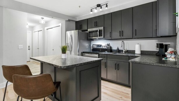 A modern kitchen with dark cabinets, stainless steel appliances, a granite countertop, and two brown leather chairs. - The Lofts of Downtown 540 N 2nd St, #207 (Clarksville)