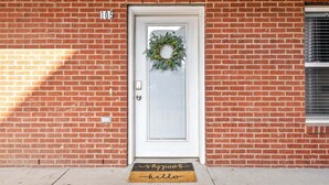 A brick building with a white door, a number "105" above it, and a doormat with "shoppe" and "hello" on it. - Loft #105 (Clarksville)