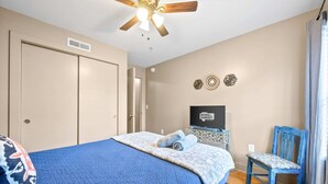 A bedroom with a bed, a ceiling fan, a TV, and a chair. - Loft #105 (Clarksville)