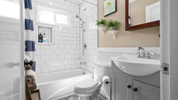 A bathroom with white tiles, a bathtub, a toilet, a sink, and a shower.