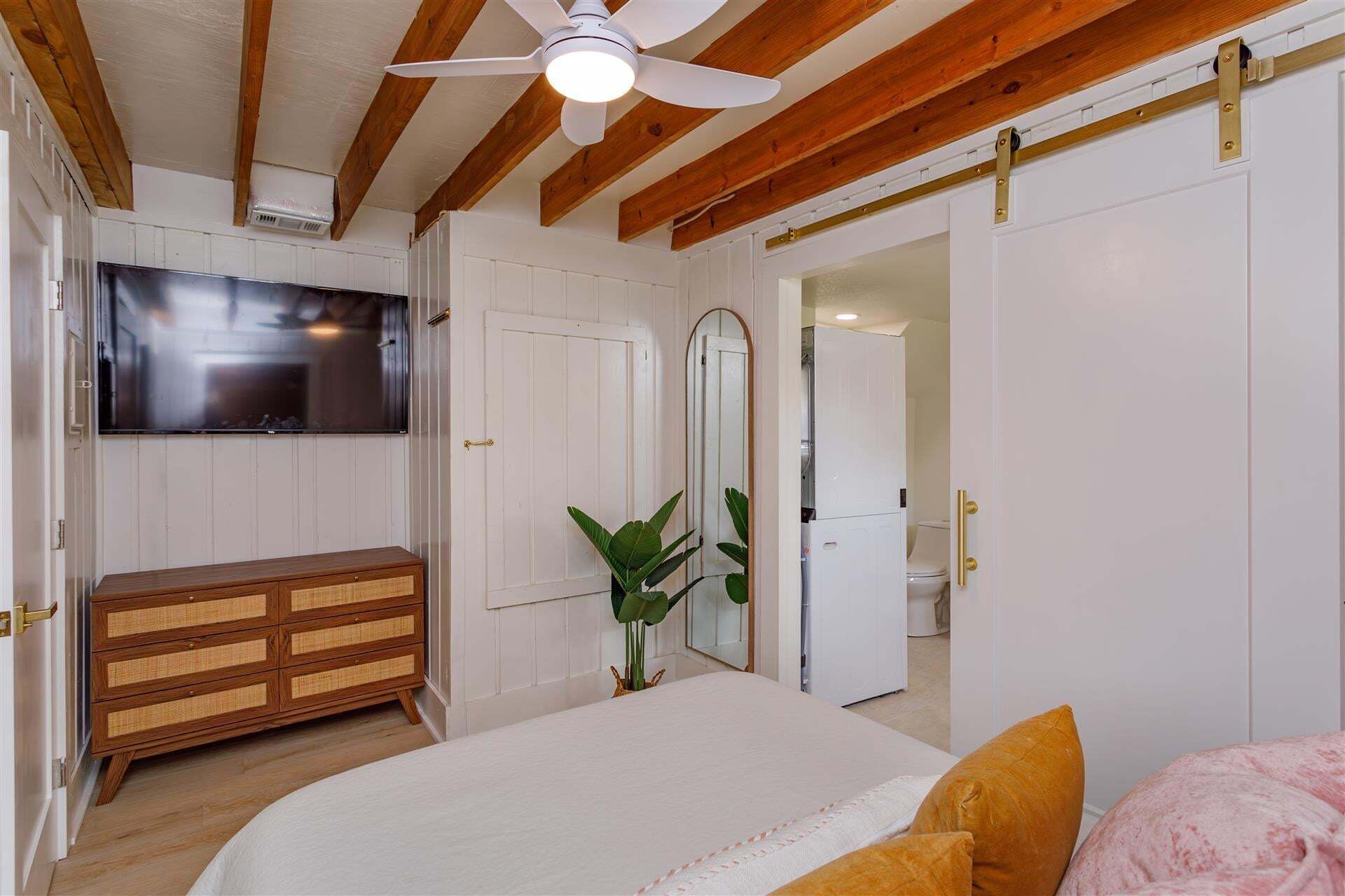 Un dormitorio con cama, cómoda, televisor y puerta corrediza que da al baño.