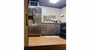 A kitchen with a stainless steel refrigerator, wooden countertop, and cabinets.