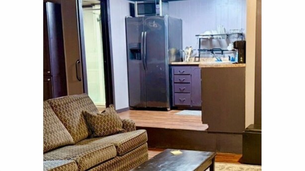A compact living space with a sofa, a small table, a kitchenette with a refrigerator and microwave, and a sliding door leading to another room.
