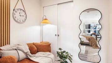 A bedroom with a bed, a bedside lamp, a wall clock, a mirror, and a plant.