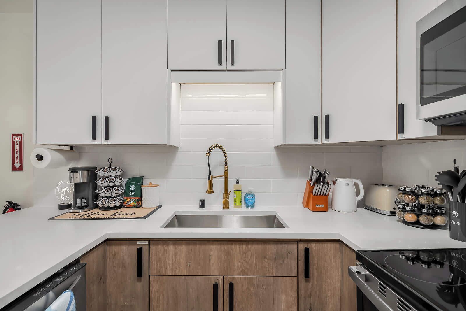 A modern kitchen with white cabinets, a stainless steel sink, a coffee bar, and a stove.