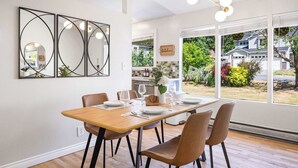 Een eetruimte met een houten tafel gedekt voor vier personen, omringd door stoelen, met een groot raam dat uitzicht geeft op de omgeving.