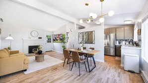 Een ruime woonkamer met een bank, een eettafel met stoelen, een open haard en een keuken met moderne apparatuur.