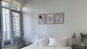 Un dormitorio con una cama grande, una mesita de noche con lámpara y una ventana con persianas.