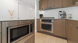 Una cocina moderna con electrodomésticos de acero inoxidable, armarios de madera y encimera blanca.