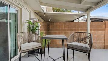 An outdoor patio with two wicker chairs and a table, a potted plant, and a brick wall.
