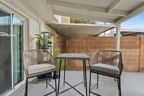 Une terrasse extérieure avec deux fauteuils en osier et une table, une plante en pot et un mur en briques.