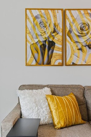 Una sala de estar con un sofá, dos cojines y dos obras de arte enmarcadas en la pared.