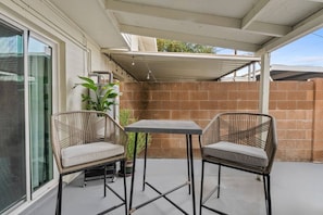 Une terrasse couverte avec deux fauteuils en osier et une table, une plante en pot et un mur en briques.