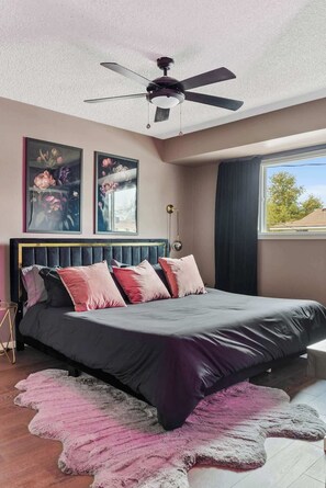 Une chambre à coucher avec un lit, un ventilateur de plafond, une fenêtre et des œuvres d’art accrochées au mur.