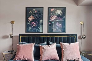 A bedroom with a dark blue upholstered headboard, a bed with pink pillows, and two framed floral paintings on the wall. - Artsy Townhouse w/ Billiards & King En Suite (Phoenix)