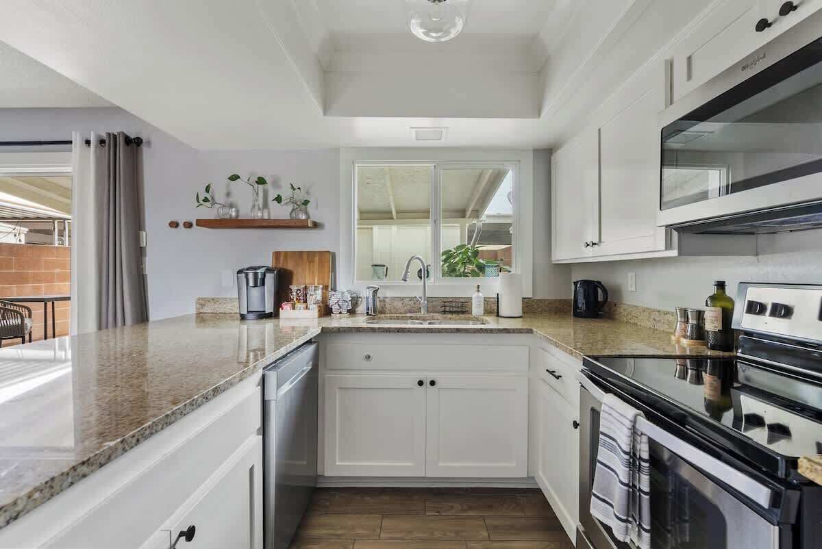 Eine moderne Küche mit weißen Schränken, einer Granitarbeitsplatte, einem eingebauten Backofen und einem großen Fenster.