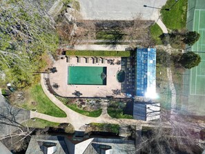 Ein Luftbild eines Sportgeländes mit Tennisplatz, umliegender Bepflanzung und einem Gebäude mit blauem Dach.