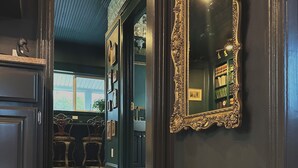 En gang med et ternet gulv, et stort, detaljeret spejl og udsigt til et rum med en bogreol og et vindue.