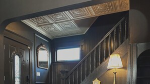 En imponerende lobby med et ternet gulv, to læderlænestole med plaider, en trappe med lampe og et dekorativt loft.