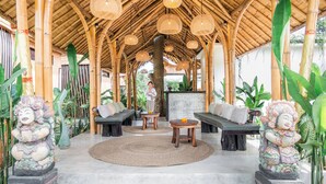 A covered outdoor seating area with bamboo structures, woven light fixtures, and traditional statues. - Sindu Village Ubud (Ubud)