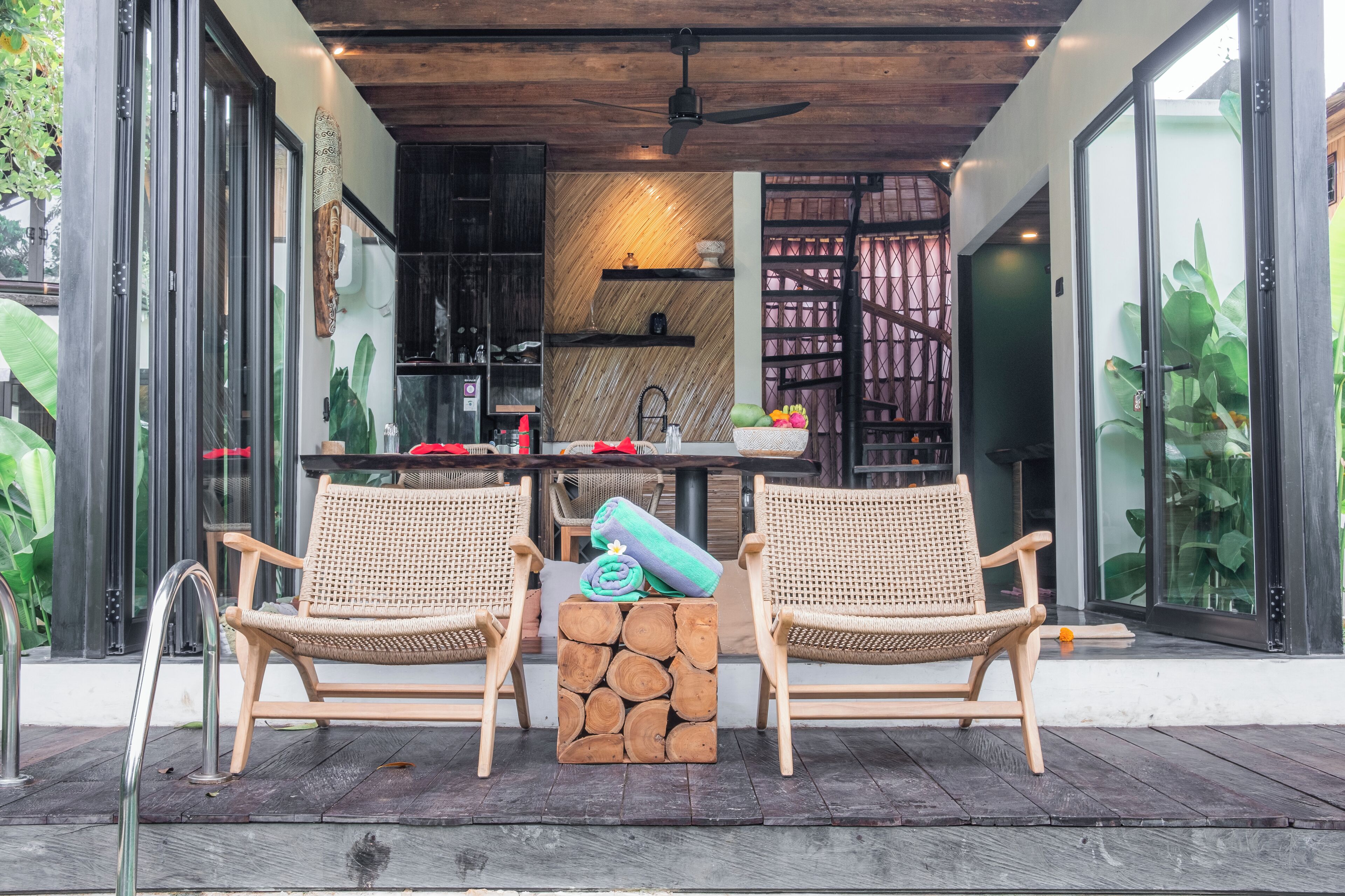 Un espacio de descanso al aire libre moderno con dos sillones de mimbre, una mesa de madera y un banco de troncos.
